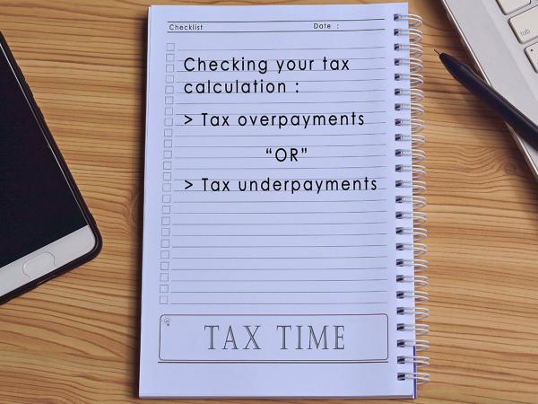pad of paper on a desk next to a keyboard and mobile phone, pad of paper reads 'CHECKING YOUR TAX CALCULATION: TAX OVERPAYMENTS OR TAX UNDERPAYMENTS'