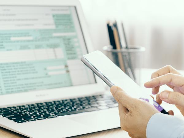 person holding a mobile phone whist using a laptop