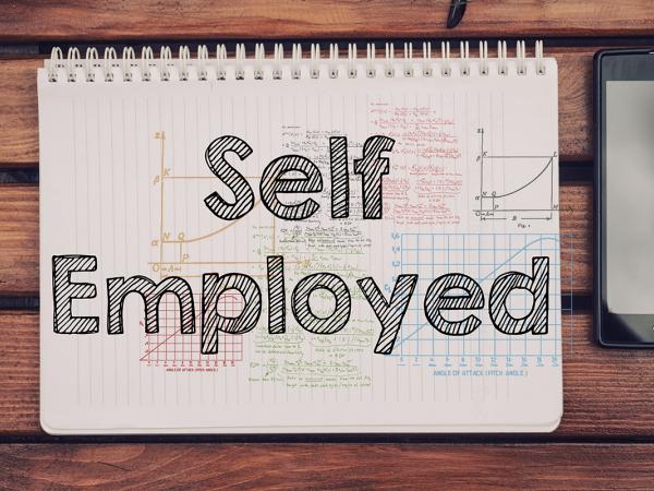 a wooden table with a mobile phone and a pad of paper with the words 'SELF EMPLOYMENT' written on it. 