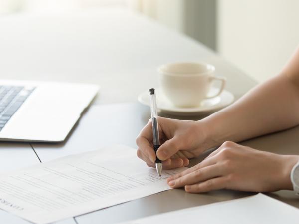 a person sat at a desk with a laptop, signing a document. 