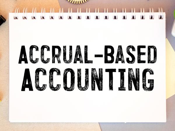 A pad of white paper with the words 'ACCRUAL-BASED ACCOUNTING' around the pad of paper various stationary can be seen. 