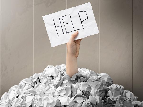 a mound of crumpled up papers with an arm sticking out holding a sheet of paper with the word 'HELP' written on it. 