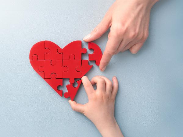 2 people completing a jigsaw puzzle, the puzzle is a red heart