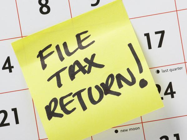 a calendar with a sticky note attached, note says in back ink 'FILE TAX RETURN!'