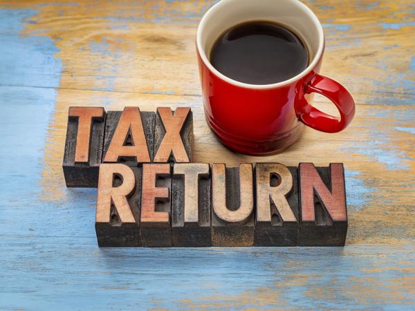 wooden letters arranged on a desk to spell 'TAX RETURN' next to this is a red cup of coffee. 