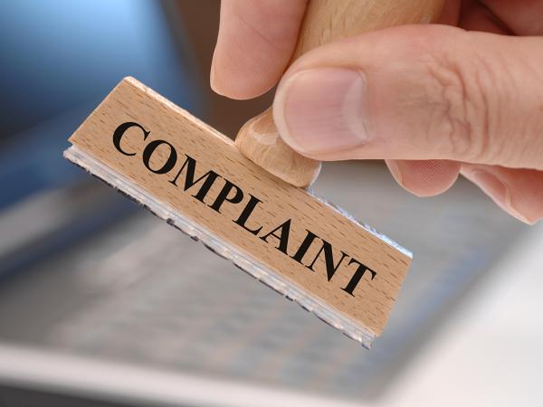 a person holding a wooden stamper, the stamper is for the word 'COMPLAINT' 