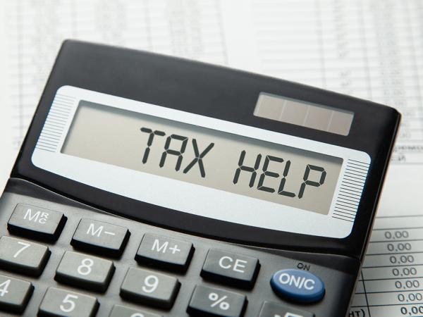 A calculator with the words 'TAX HELP' on the screen, next to the calculator is a pen, the background is made up of paperwork. A calculator with the words 'TAX HELP' on the screen, next to the calculator is a pen, the background is made up of paperwork.