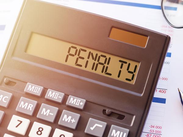 a calculator with the word 'PENALTY' typed on it. next to the calculator a pair of glasses and a pen can be seen. the background is paperwork. 