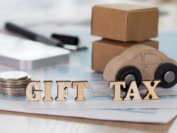 a desk showing paperwork, coins, a phone and a wooden car with wooden letters that spell out 'GIFT TAX' 
