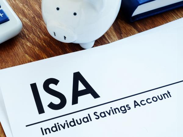 a desk with a calculator, a piggy bank, pens, a calculator and a sheet of white paper with the words 'ISA INDIVIDUAL SAVINGS ACCOUNT' written on it.