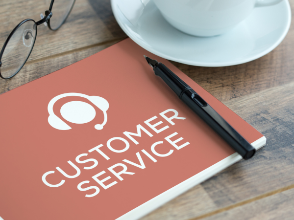 a booklet titled 'CUSTOMER SERVICE' on a desk besides a pair of glasses and a cup of tea.