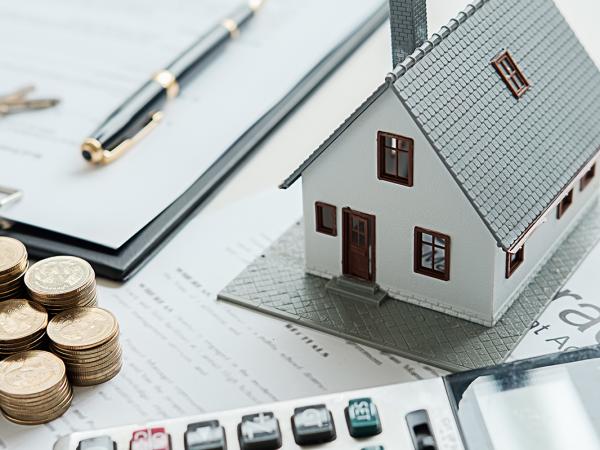 a miniature house, stacks of coins, keys and paperwork sat on a desk.
