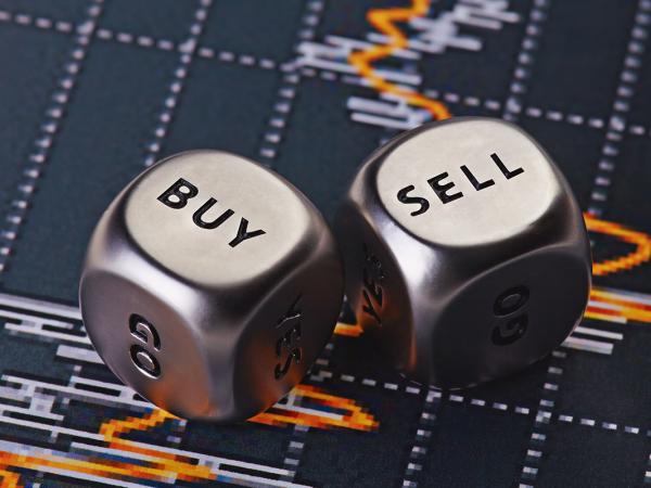 two metal dice with the words 'BUY' and 'SELL' on them, in the background a graph can be seen. 