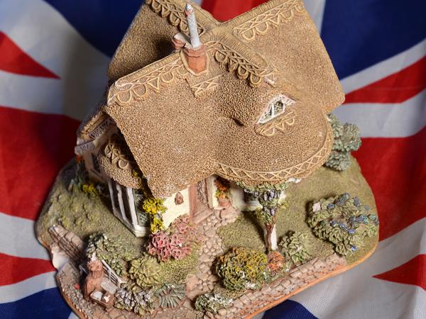 background is the UK flag, on top of this is a model of a traditional English cottage
