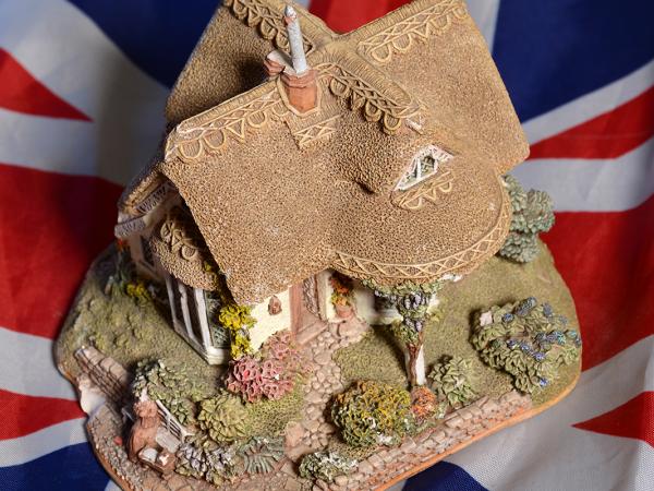 background is the UK flag, on top of this is a model of a traditional English cottage