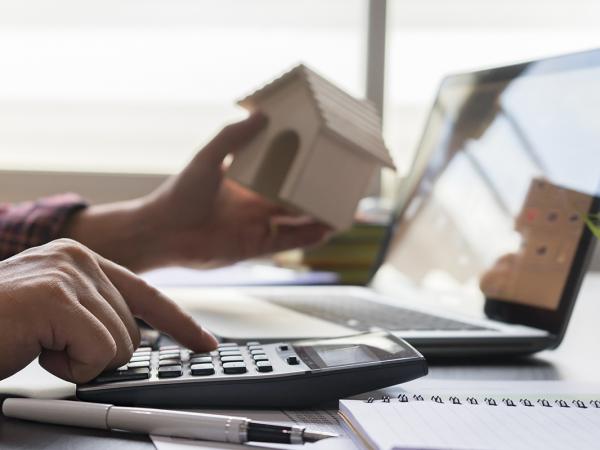 a person doing calculations on a calculator whilst holding a miniature house