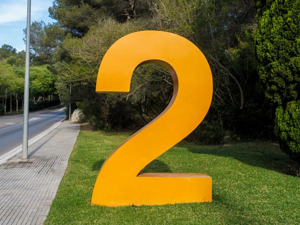 Background of a blue shy and green grass and trees next to a road. On the grass sits a large orange number 2.