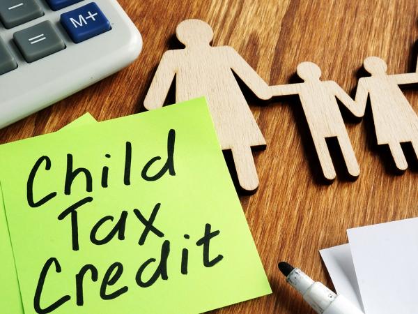 wooden figures of a family with 2 children, a green post it note can be read saying 'CHILD TAX CREDIT'. 