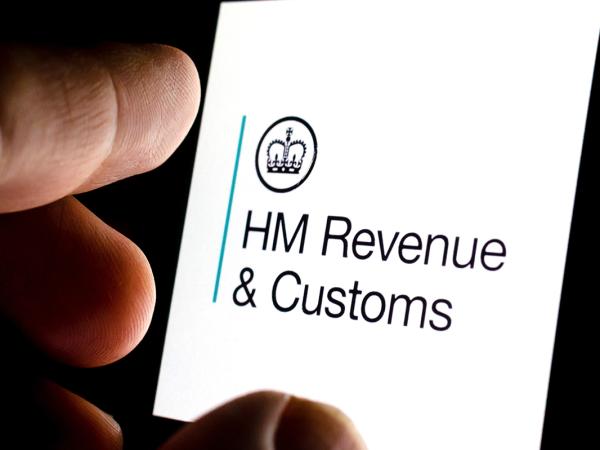 A person looking at their smartphone, the screen shows the HMRC logo. 'HM REVENUE & CUSTOMS'. 