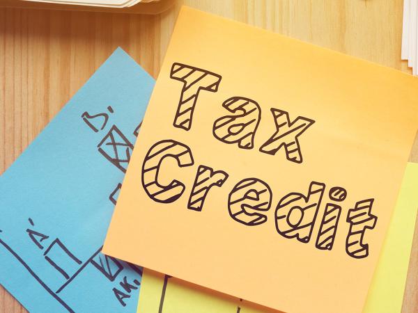 A stack of various coloured, used post-it notes, the top one is orange and it reads 'TAX CREDIT'.