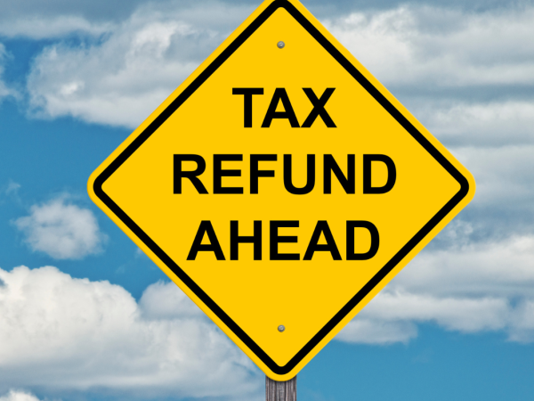 A blue sky with a yellow traffic sign with the words 'TAX REFUND AHEAD' in black text. 