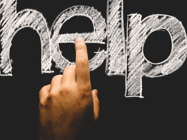 a person pointing to the word 'HELP' written on a chalkboard
