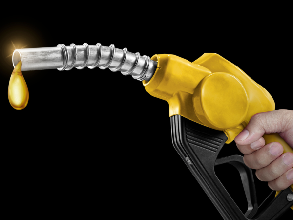 A person holding a fuel pump nozzle, the end of the nozzle is dripping with liquid gold. 