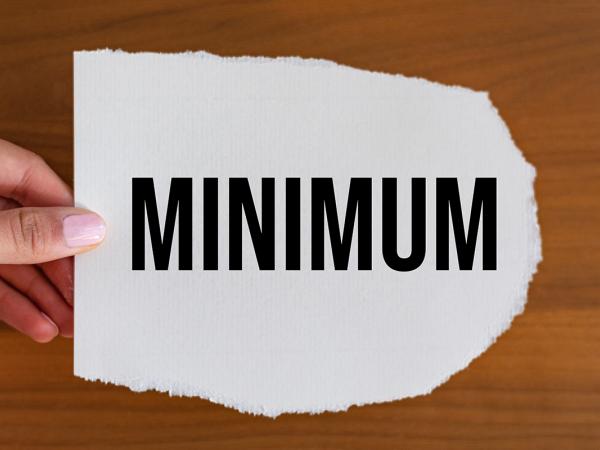 A person holding a piece of white paper with the word 'MINIMUM' typed in black text.
