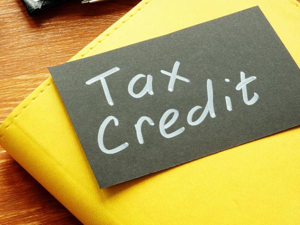 A black card showing the words 'TAX CREDIT' in white writing, the card is sat on top of a yellow notebook on a desk next to a computer keyboard. 