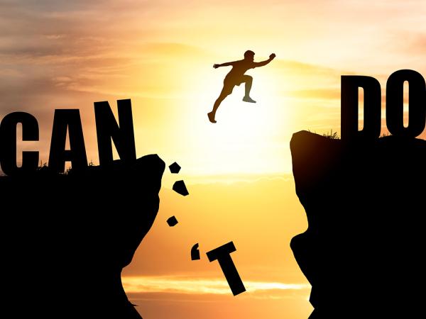 A person jumping from one cliff edge to another, the words 'I CAN DO IT' can be seen across the cliffs. The jump has knocked the 'T' from 'CAN'T'.