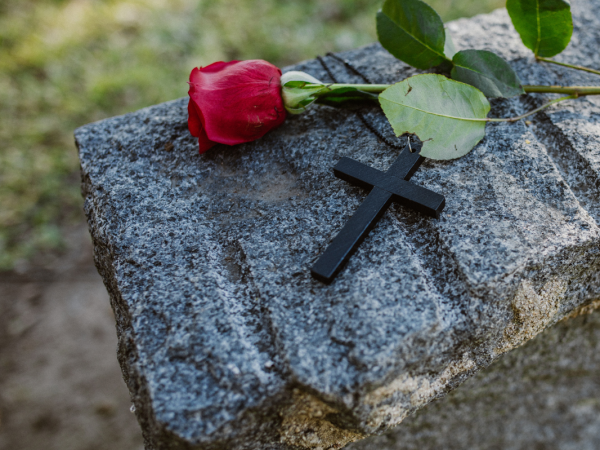 A gravestone with a black cross and a red rose laid on top A gravestone with a black cross and a red rose laid on top