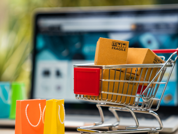 A laptop, a mini shopping trolley filled with goods and colourful shopping bags
