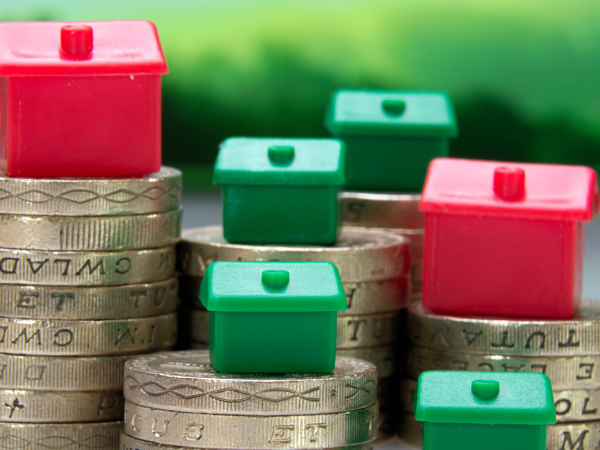 Tiny monopoly houses on top of piles of pound coins. 