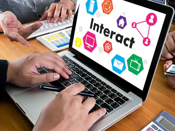 A group of people sitting around a laptop that has the word 'INTERACT' on the screen.