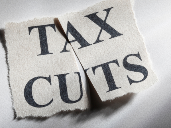 A scrap of paper with the words 'TAX CUTS' printed in black text, this paper has been cut in half.