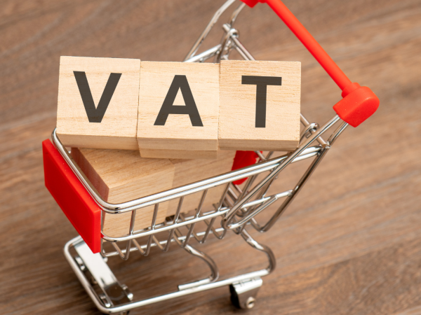 tiny shopping trolley with wooden lettered blocks inside, together they spell out the word 'VAT'. 