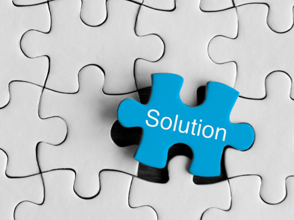 A plain white jigsaw with one piece left to place, the final piece is a blue piece with the word 'SOLUTION' on it in white text.