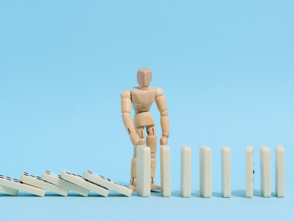 a wooden figure picking up fallen domino's