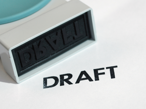 A hand stamper and the word 'DRAFT' stamped onto a white surface