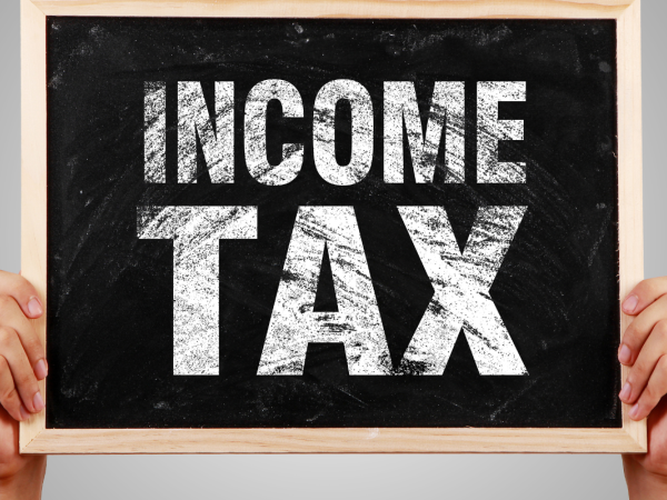 A person holding up a small chalkboard with the words 'INCOME TAX' written on it in white chalk. 