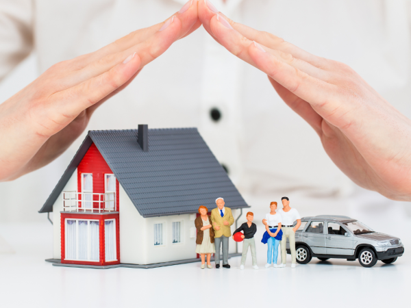A person's hands covering a model home, car and tiny family to protect them. A person's hands covering a model home, car and tiny family to protect them.