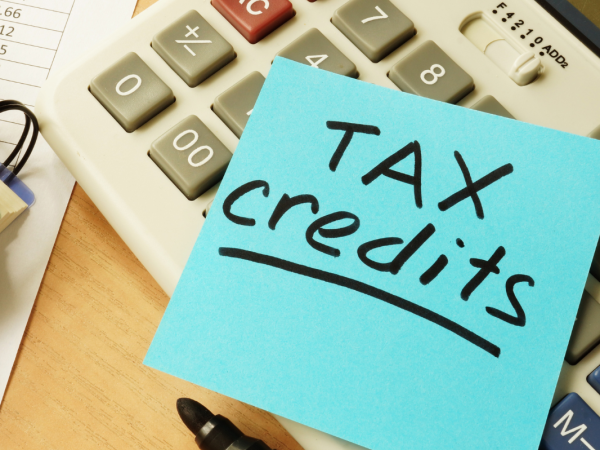 a blue post it note with the words 'TAX CREDITS' written on it in black pen, also on the desk is a notebook and a calculator. 