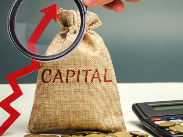 A brown sack with the word 'CAPITAL' on it, a calculator, a red arrow pointing upwards and a magnifying glass. A brown sack with the word 'CAPITAL' on it, a calculator, a red arrow pointing upwards and a magnifying glass.