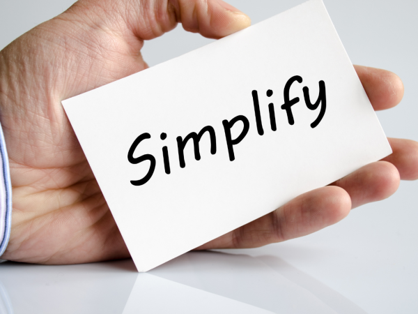 A person holding a white card with the word 'SIMPLIFY' written in black text