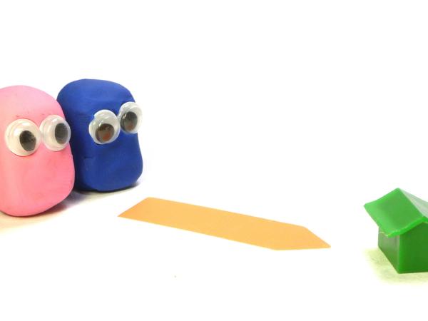 2 people made from play-doh with googly eyes (one pink, one blue), following an arrow marked on the floor towards a tiny green house. 