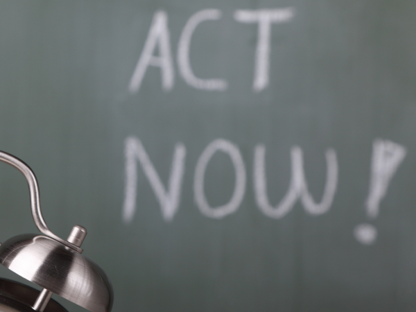 A bedside alarm clock sat in front of a chalk board, the board reads 'ACT NOW!' A bedside alarm clock sat in front of a chalk board, the board reads 'ACT NOW!'
