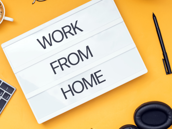 A yellow background with a keyboard, headphones, hot beverage, pen and a paper that reads 'WORK FROM HOME' A yellow background with a keyboard, headphones, hot beverage, pen and a paper that reads 'WORK FROM HOME'