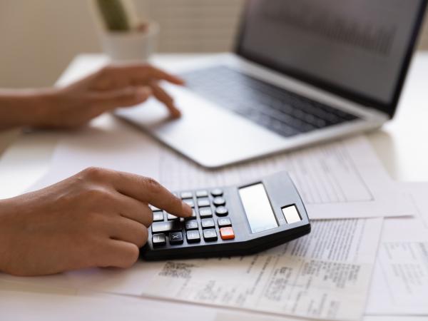 Close up of young female electronic bank client using calculator in paperwork with accounts bills before providing payment online by laptop Close up of young female electronic bank client using calculator in paperwork with accounts bills before providing payment online by laptop