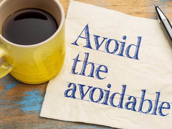 A yellow cup, a napkin and a pen on a table, the napkin has been written on and says 'AVOID THE AVOIDABLE''