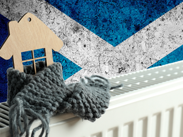 A white metal radiator with a wooden house on top wrapped in a scarf, behind the Scottish flag can be seen. 